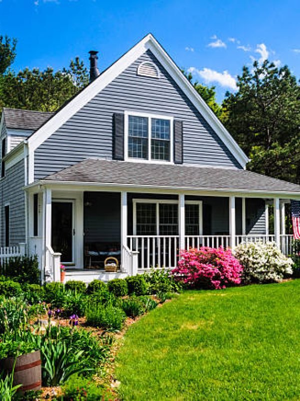 An American flag flies from the open porch and gardens surround a small  single family home on a Spring afternoon on Cape Cod on the Massachusetts coast. (Property release attached)